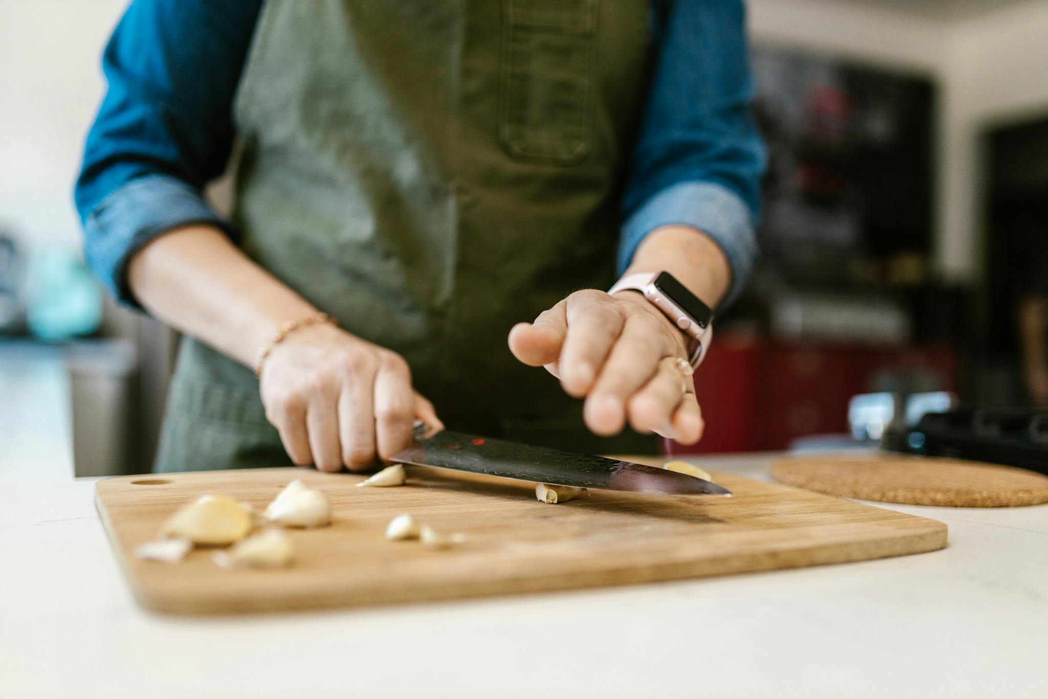 A woman slicing garlic on a wooden cutting board, showcasing culinary preparation.