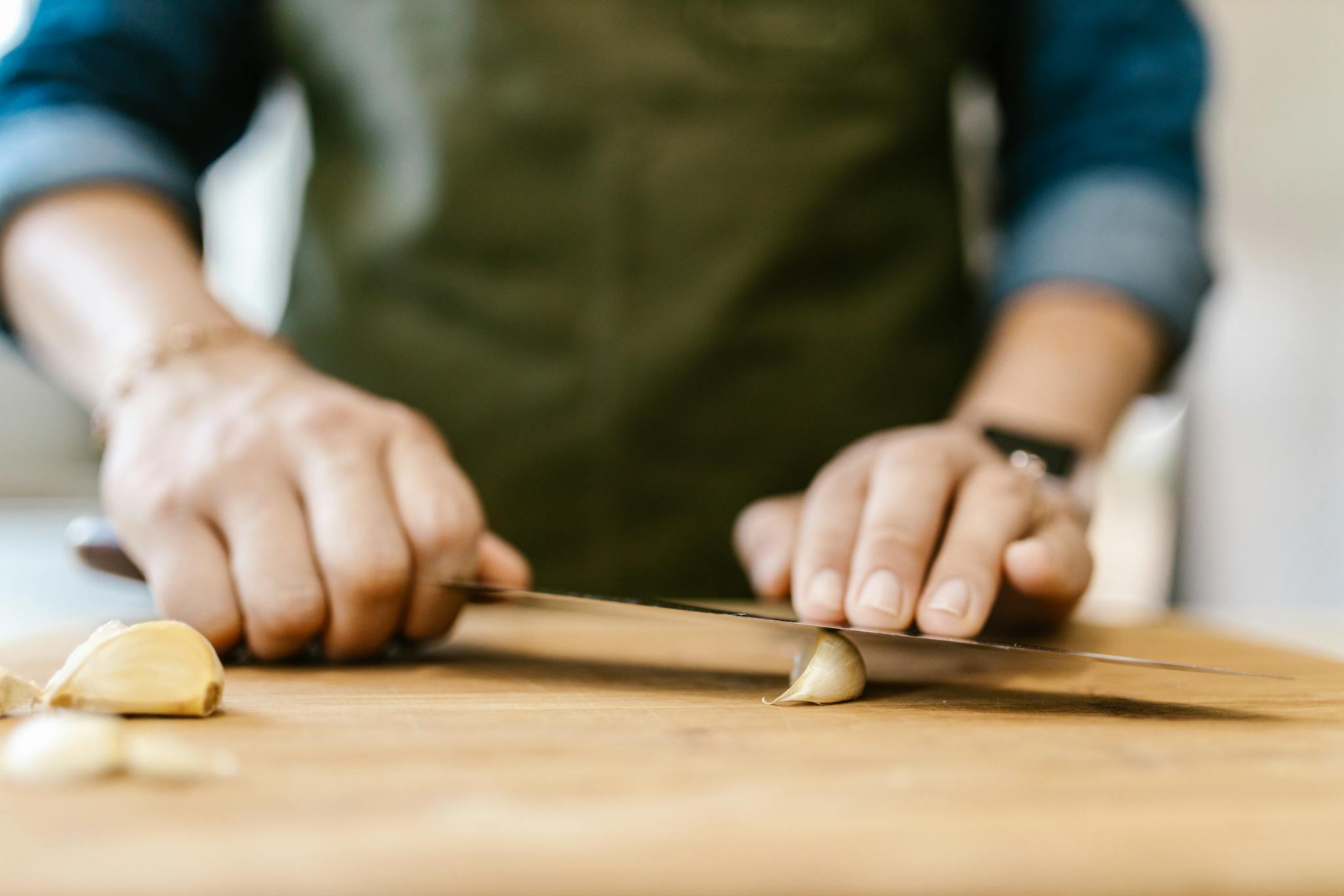 Close-up of a person slicing garlic on a wooden cutting board, emphasizing cooking preparation.