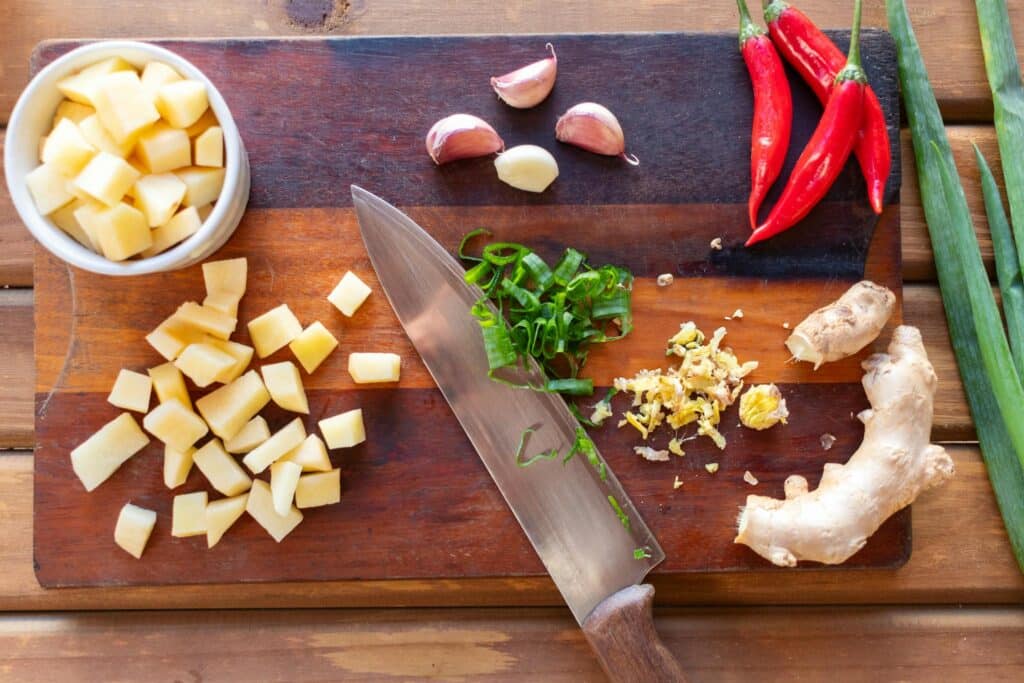 Vibrant cutting board scene with diced potatoes, chili peppers, ginger, and garlic.