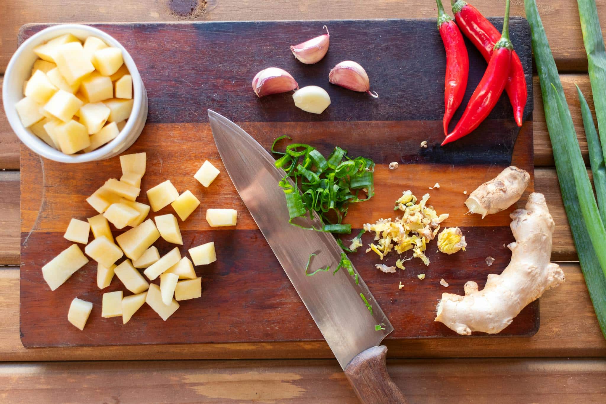 Vibrant cutting board scene with diced potatoes, chili peppers, ginger, and garlic.